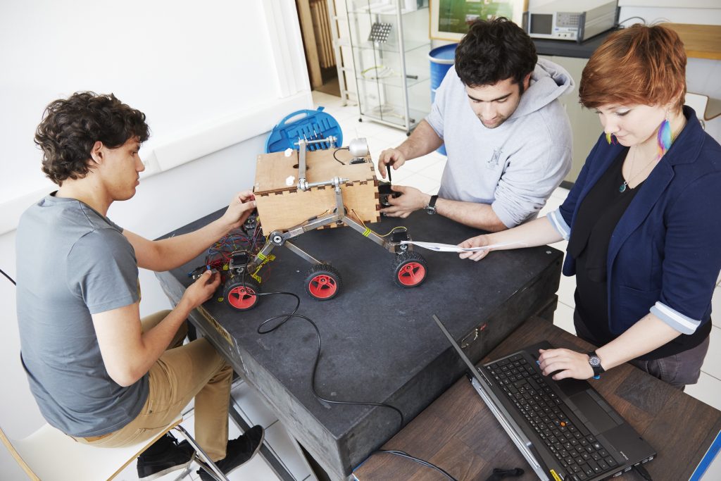 3 étudiants travaillent sur un prototype de robot à 6 roues