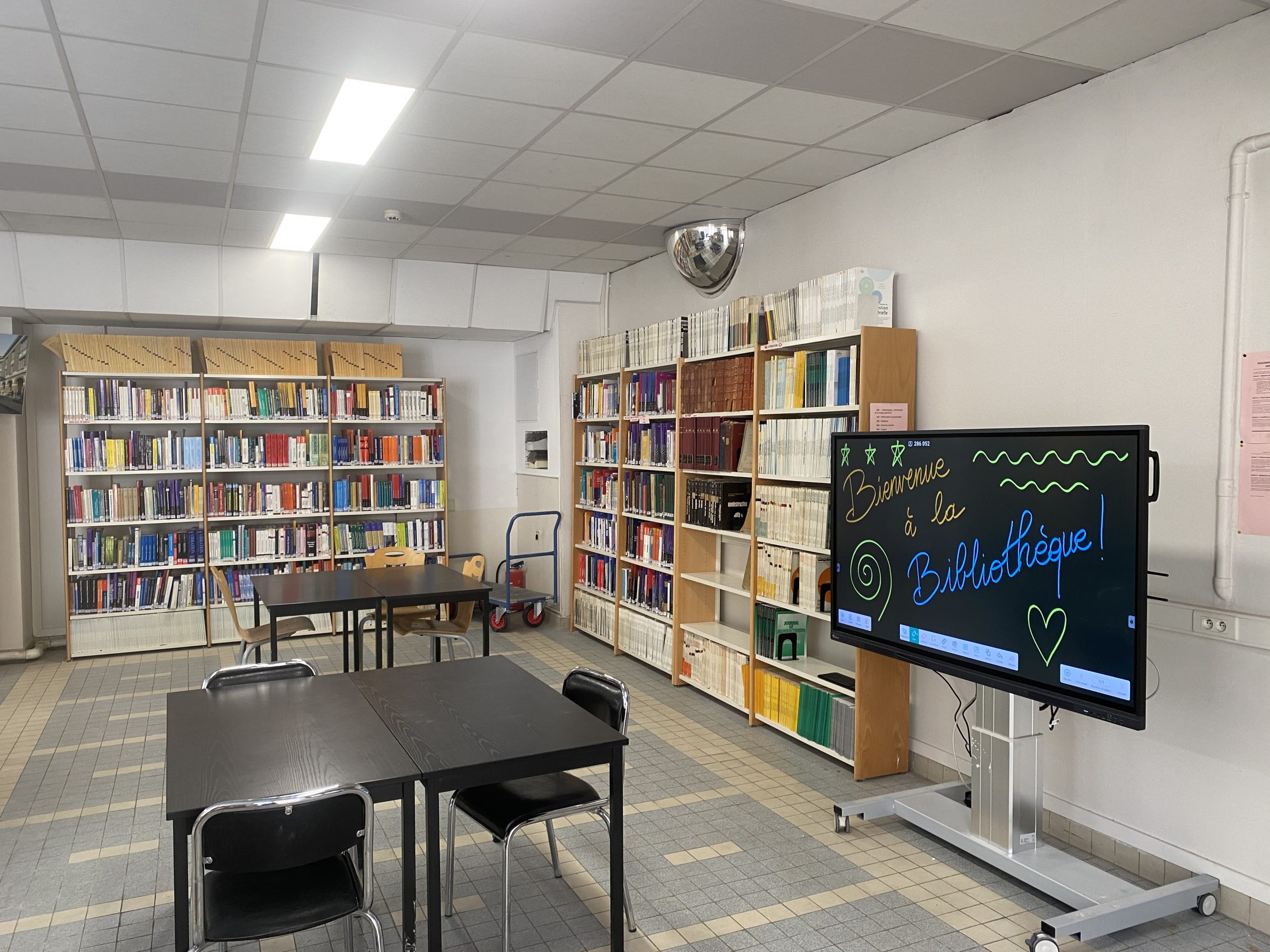 Image de bibliothèque avec un tableau numérique sur lequel il est écrit "Bienvenue à la bibliothèque"